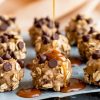 The image highlights several Chocolate Caramel Oatmeal Cookies placed on parchment paper. A drizzle of thick caramel sauce is being poured over one cookie, enhancing its glossy coating and adding a decadent touch.