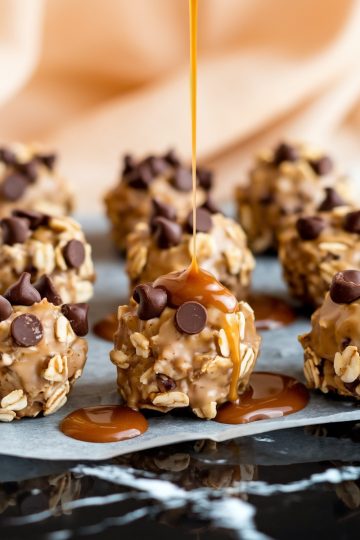 The image highlights several Chocolate Caramel Oatmeal Cookies placed on parchment paper. A drizzle of thick caramel sauce is being poured over one cookie, enhancing its glossy coating and adding a decadent touch.