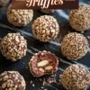 Close-up of no-bake chocolate hazelnut truffles arranged on a dark marble surface. Each truffle is coated in finely chopped hazelnuts, with one cut open to reveal a rich chocolate ganache filling and whole hazelnuts inside. The text overlay reads "No-Bake Chocolate Hazelnut Truffles" in bold lettering.