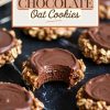 Close-up of no-bake chocolate oatmeal cookies arranged on a black marble surface. A cookie with a bite taken out reveals its soft chocolate layer and chewy oatmeal texture. Text overlay reads, "No-bake chocolate oat cookies."