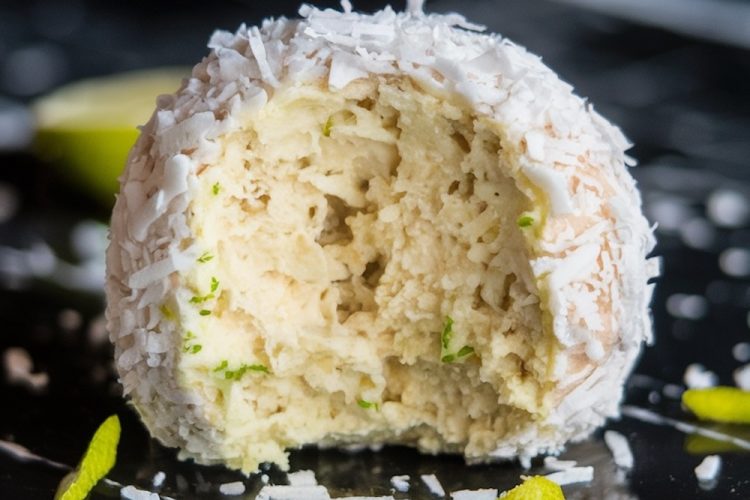 A close-up of a single coconut lime ball with a bite missing. The ball is coated in shredded coconut and lime zest, resting on a glossy black surface. The text overlay reads "Zesty Coconut Lime Balls" in bold green and white font.