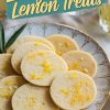 A close-up of "Zesty Cashew Lemon Treats," showcasing golden round cookies on a decorative porcelain plate, sprinkled with fresh lemon zest. The background includes soft lighting and blurred glasses of refreshing beverages.