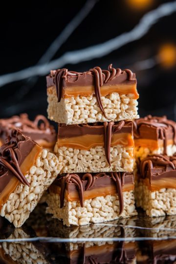 Stacked chocolate caramel Rice Krispie treats on a cooling rack, featuring glossy caramel and chocolate layers dripping slightly. Crisp rice cereal base adds contrast to the rich toppings. Keywords: stacked Rice Krispie treats, caramel chocolate layers, cooling rack, dessert close-up.