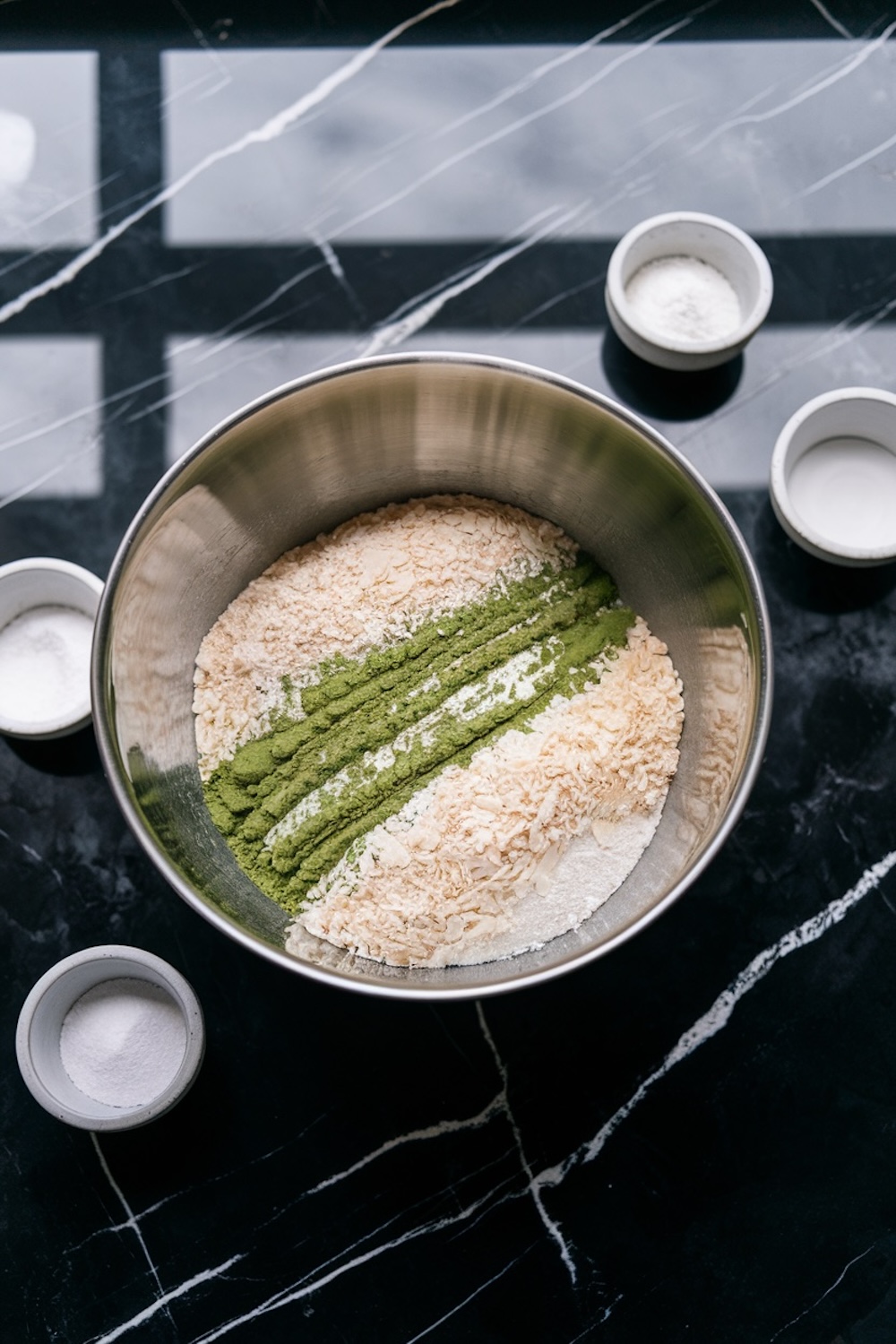 A mixing bowl with dry ingredients for matcha coconut balls, including rolled oats, matcha powder, and shredded coconut, arranged in clean lines to highlight the vibrant green matcha against the other textures.