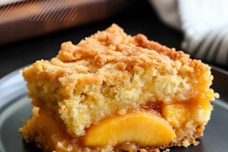A close-up of a single slice of peach dump cake served on a black plate. The warm peaches, syrupy filling, and crispy buttery topping create a visually appealing dessert perfect for casual or holiday servings.