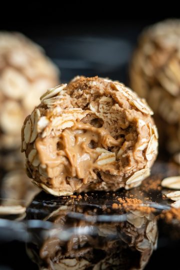 Detailed shot of a peanut butter-filled oatmeal energy ball with a bite taken out, revealing a creamy, rich peanut butter center surrounded by oats and cinnamon.