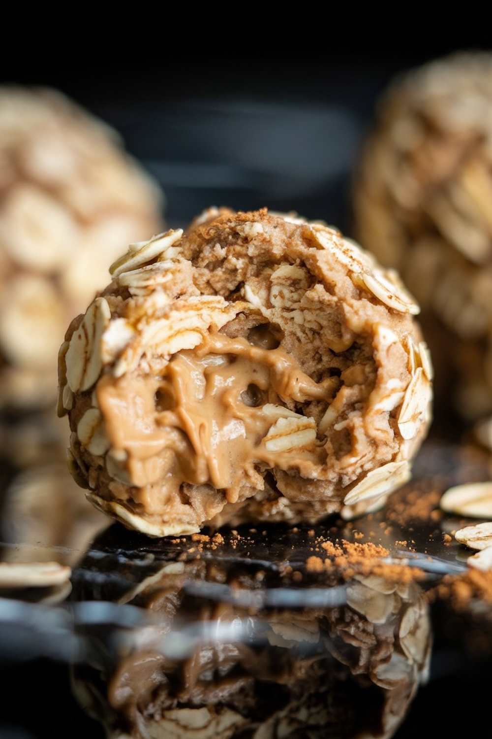 Detailed shot of a peanut butter-filled oatmeal energy ball with a bite taken out, revealing a creamy, rich peanut butter center surrounded by oats and cinnamon.