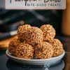 A close-up shot of pumpkin spice balls stacked on a white plate over a reflective black marble surface. The balls have a textured golden coating, emphasizing their bite-sized shape and detailed crumbly exterior.