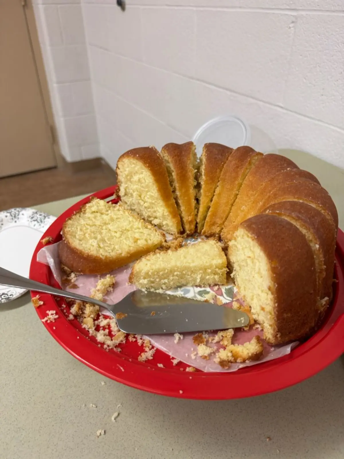 Sliced classic vanilla bundt cake on a red plate, served at a meeting by Alissa. The cake has a golden crust and soft yellow interior, with visible crumbs and a serving knife nearby.