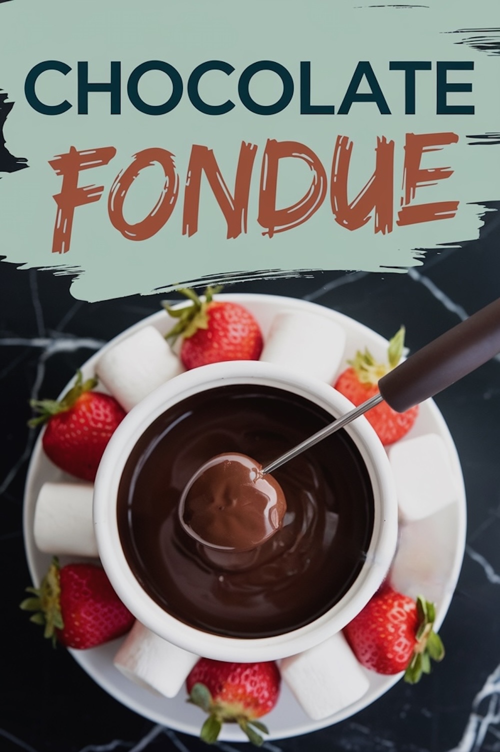 Overhead view of a bowl filled with rich, melted chocolate fondue surrounded by a variety of dippers, including vibrant red strawberries and fluffy white marshmallows, all arranged on a white plate. A fondue fork dips a piece of fruit into the smooth, glossy chocolate. Text overlay reads “Chocolate Fondue.”