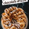 A close-up of a finished funnel cake on a white plate, drizzled with chocolate sauce and sprinkled with powdered sugar. The background features a dark, glossy surface with scattered powdered sugar for added contrast.