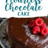Flourless chocolate cake covered in a smooth chocolate ganache, decorated with powdered sugar and a cluster of fresh raspberries on top, displayed on a ceramic plate with a dark marble background.