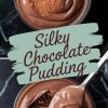 A close-up of chocolate pudding in a bowl, topped with a sprinkle of cocoa powder and a piece of dark chocolate, with a spoon scooping the creamy dessert to showcase its glossy finish.