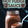 A glass jar filled with creamy homemade hot fudge sauce, with a silver spoon drizzling the rich chocolate sauce. The text overlay reads, “Homemade Hot Fudge Sauce,” on a dark marble background.