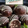A plate of chocolate mint truffles stacked elegantly with white chocolate drizzle and fresh mint leaves. A sliced truffle in the foreground reveals the textured mint chocolate filling, with the text overlay: “Homemade Mint Choco Balls – DIY in Minutes.”