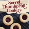 A plate of sorrel thumbprint cookies with jam-filled centers and powdered sugar on top, positioned under the bold text “Sorrel Thumbprint Cookies” in maroon over a cream brushstroke background, with additional cookies on a cooling rack in the background.