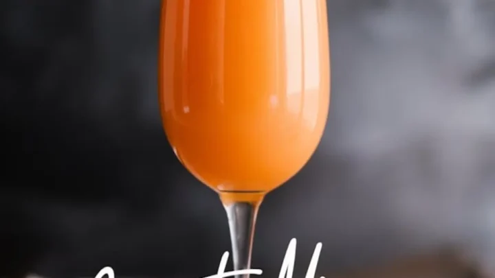 A single champagne flute filled with bright orange carrot mimosa placed on a wooden surface with a dark, blurred background. The stylish typography below the glass reads “Carrot Mimosa” and “elegant champagne flute,” enhancing the sophisticated presentation.