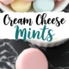 A Pinterest image featuring pastel pink, blue, and yellow cream cheese mints in a white bowl. The text “Cream Cheese Mints” is displayed in bold, elegant script. A close-up of a single pink mint rests on a black marble surface, showcasing its smooth, glossy texture.