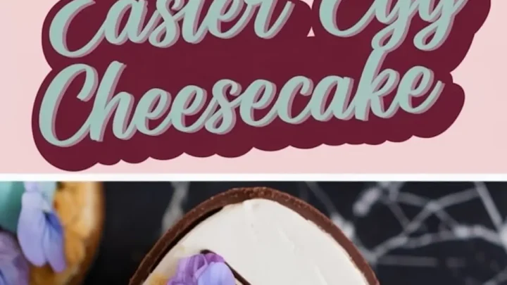 A close-up of an Easter egg cheesecake inside a chocolate shell, filled with smooth white cheesecake, topped with crushed cookie crumbs, pastel-colored mini eggs, edible purple flowers, and a drizzle of chocolate. A pink banner in the middle reads "Easter Egg Cheesecake" in decorative lettering.