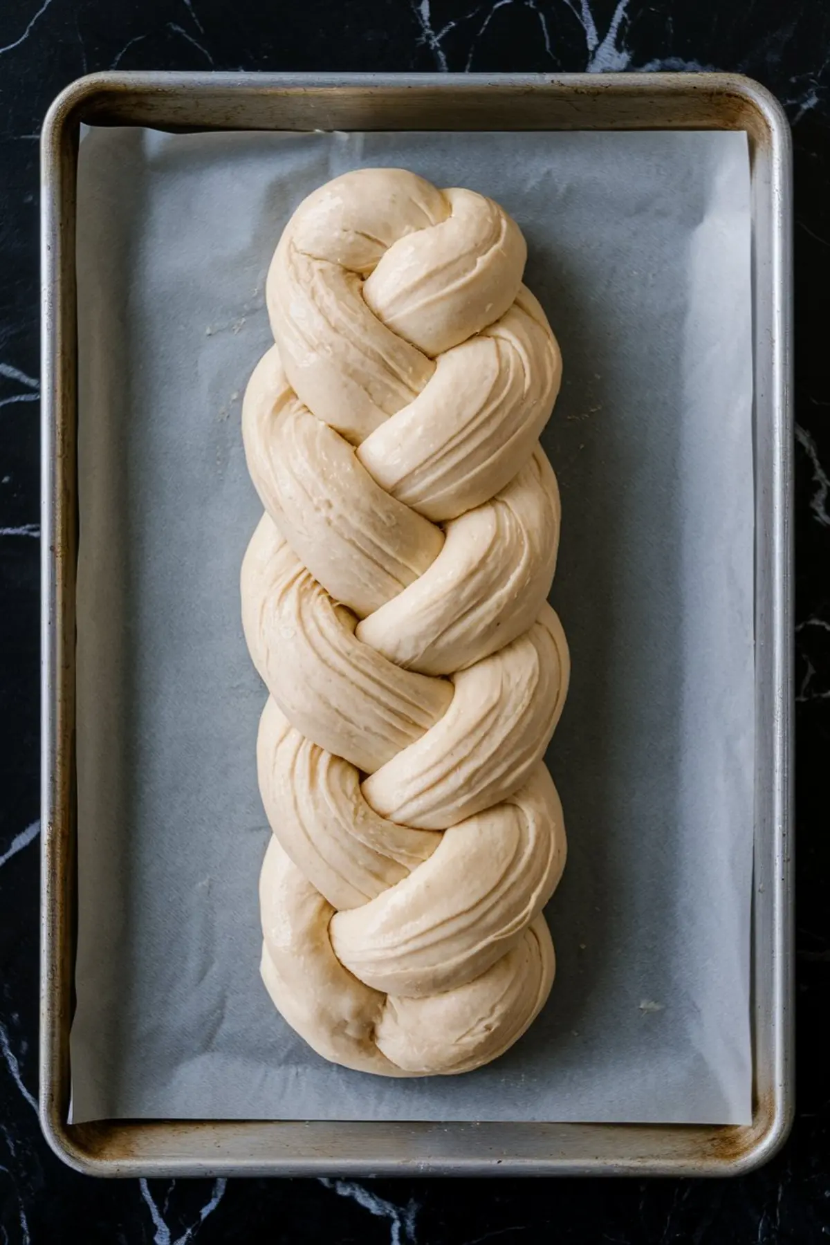 Unbaked braided dough loaf placed on a parchment-lined baking sheet, ready for the oven.