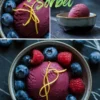 Collage of berry lemonade sorbet in ceramic bowls, topped with lemon peel spirals and surrounded by fresh blueberries and raspberries, with one image showing a side profile and the others highlighting texture and garnish.