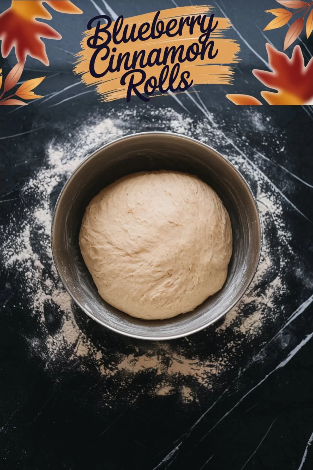A top-down view of a round dough ball in a metal mixing bowl, resting on a floured black marble surface. A text overlay with an autumn-themed design says “Blueberry Cinnamon Rolls.”