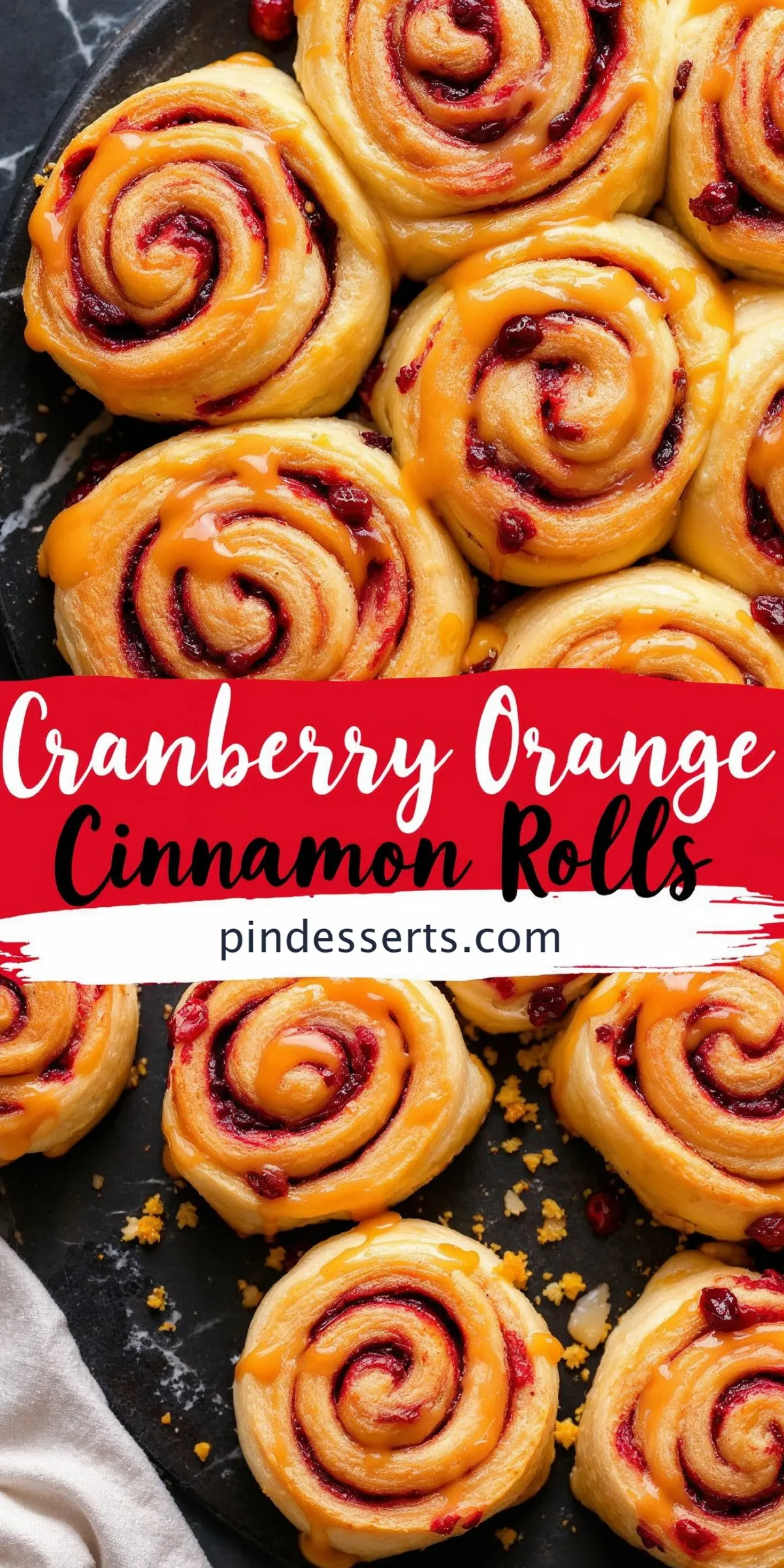 A tray of golden brown cranberry orange cinnamon rolls with a glossy orange glaze drizzled over the swirls of cranberry filling. The text “Cranberry Orange Cinnamon Rolls” and “pindesserts.com” is displayed in bold lettering.