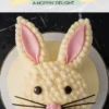 A close-up of an Easter bunny-shaped cake decorated with fluffy buttercream, pink fondant ears, chocolate button eyes, and black licorice whiskers. The cake is placed on a white plate with a black marble background. A pastel-themed text overlay reads “Easter Bunny Cake - a hoppin’ delight.”