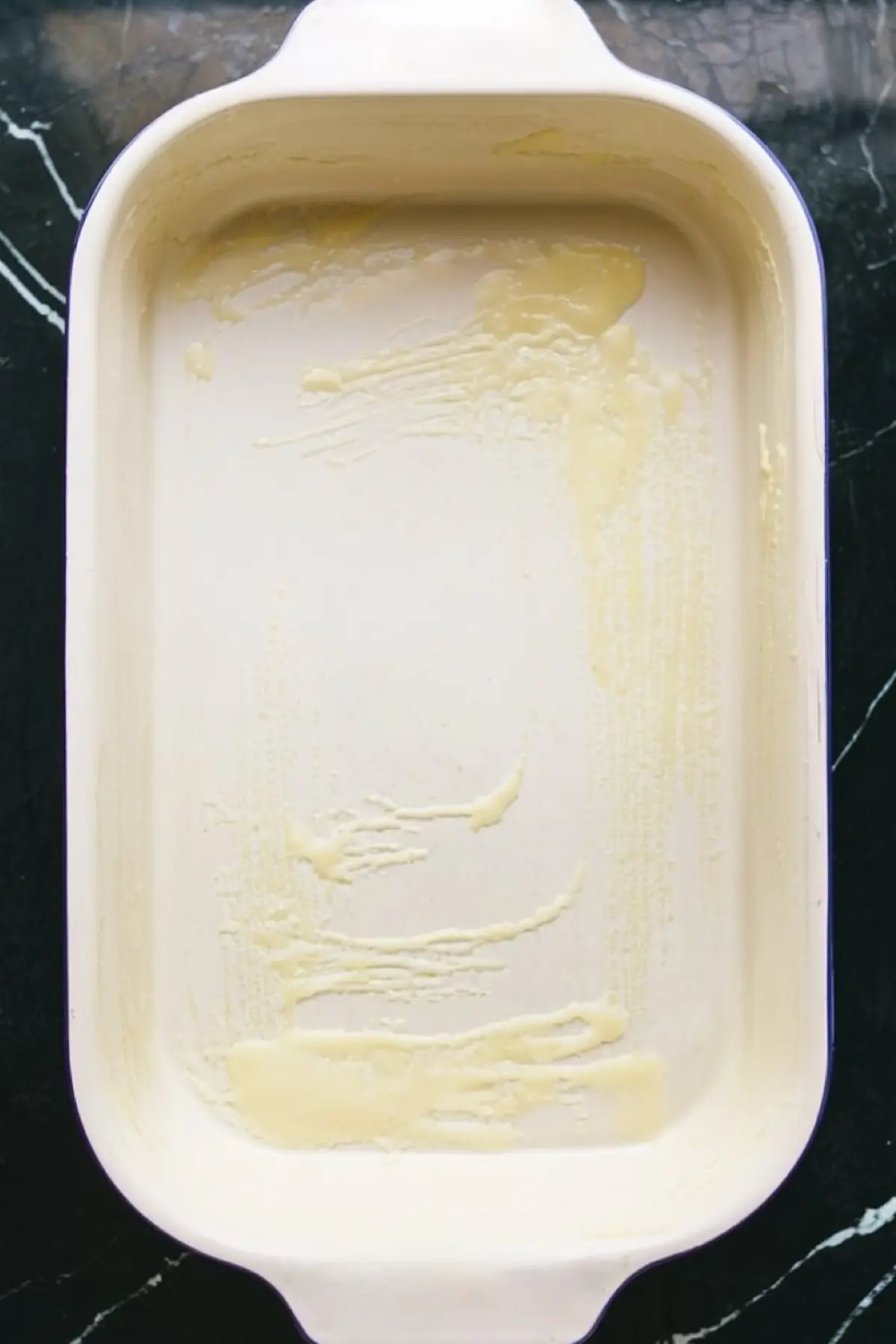 An empty white baking dish is lightly greased with butter, prepared for layering ingredients in a lemon dessert recipe.