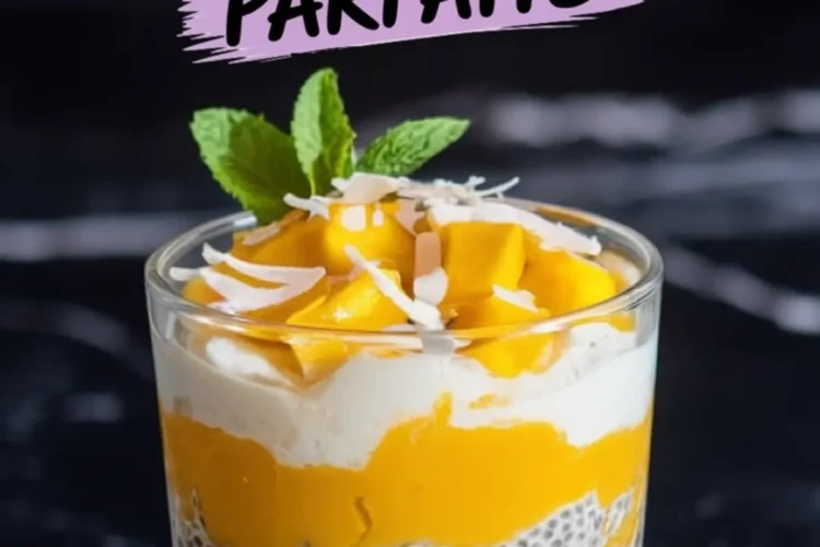 Glass of mango coconut chia pudding parfait topped with fresh mango chunks, shredded coconut, and a mint sprig, set against a black marble background.