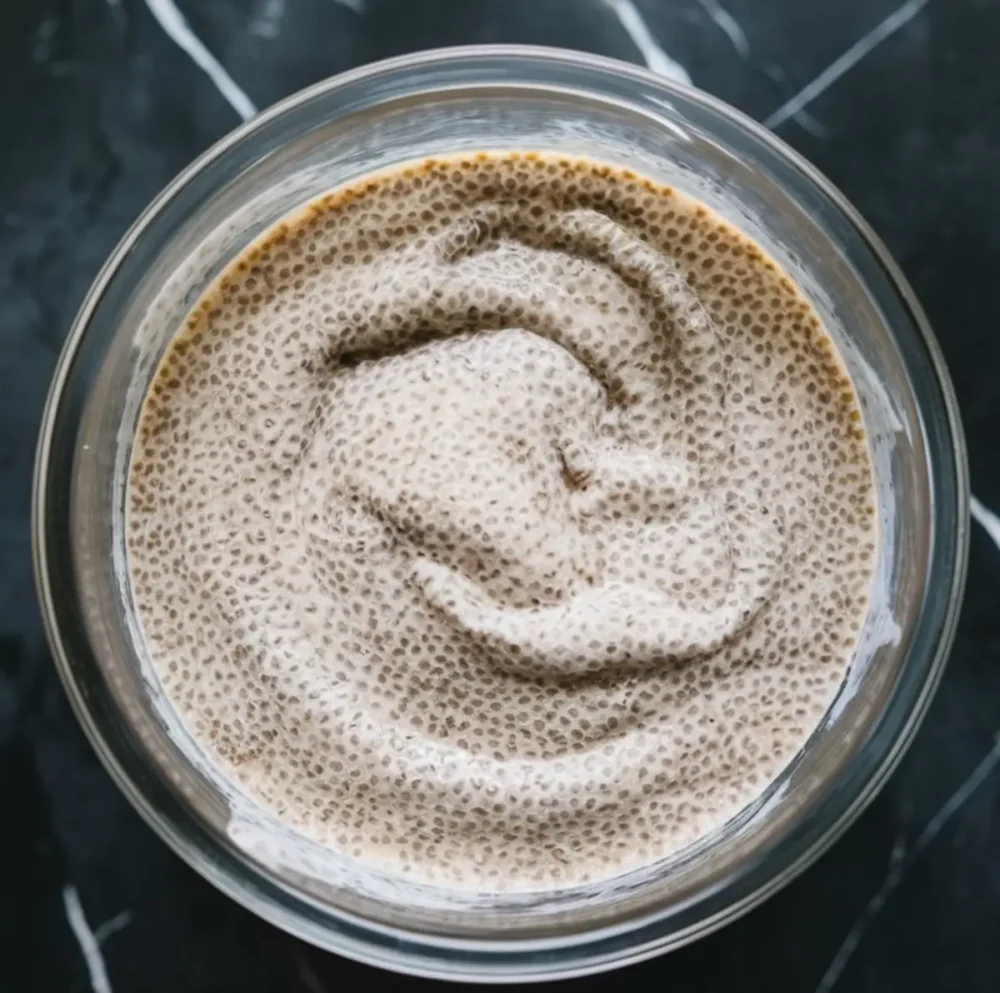 Smooth chia seed pudding mixture in a glass bowl, viewed from the top with visible hydration and gel texture.