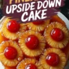 A freshly baked pineapple upside-down cake with caramelized pineapple rings and glossy red cherries, glistening with syrup. The cake sits on a white plate, with a bold text overlay reading “Pineapple Upside Down Cake.”