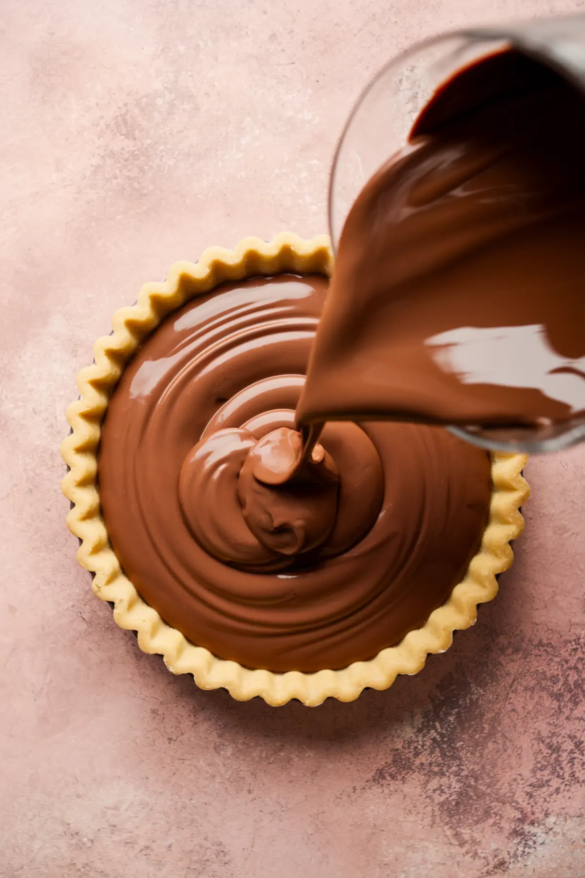Smooth chocolate ganache being poured into a baked tart shell, creating rich swirls on the surface of the dessert.