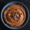 Smooth chocolate hummus topped with dark chocolate chips served in a matte blue bowl on a black marble surface.