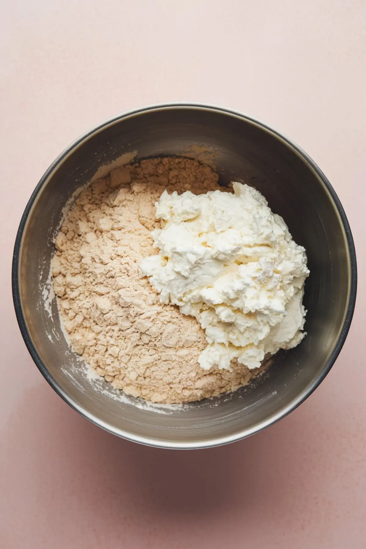 Close-up of a metal bowl containing flour and a large scoop of cottage cheese, showing the start of mixing for biscuit dough.