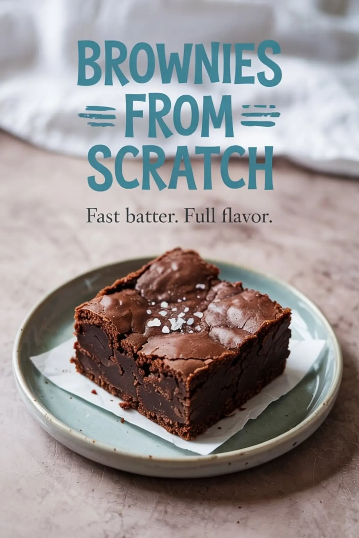 Close-up of a single fudgy brownie topped with flaky sea salt on a parchment-lined plate with bold text overlay reading “Brownies From Scratch – Fast batter. Full flavor.”