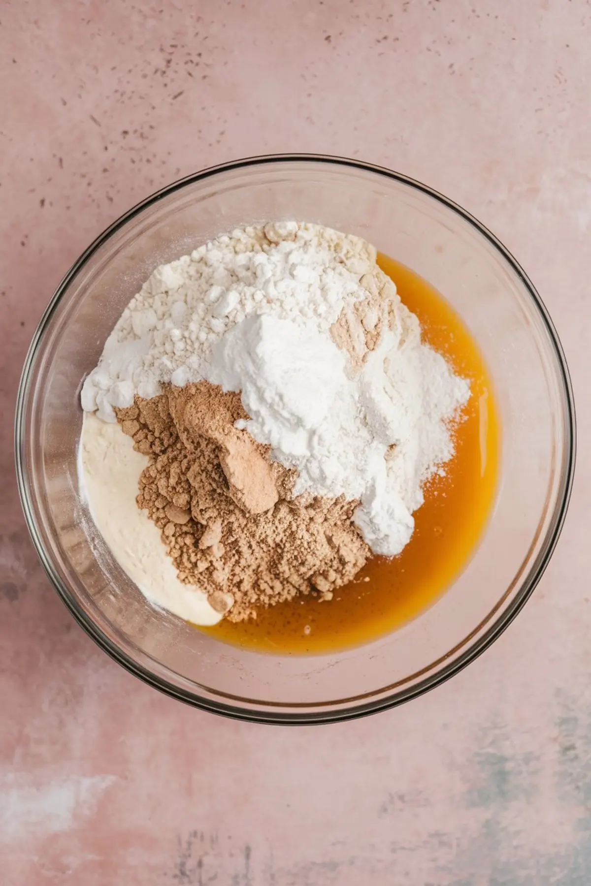 Mixing bowl filled with flour, brown sugar, baking powder, and wet ingredients like peanut butter and melted butter, just before combining into cookie dough.