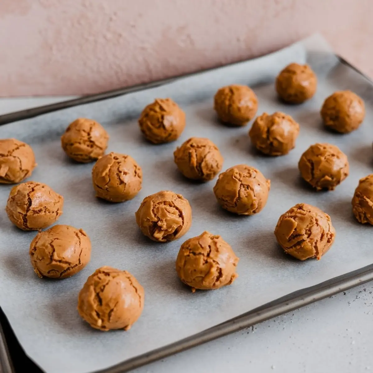 Unbaked peanut butter cookie dough balls evenly spaced on a parchment-lined baking sheet, ready for oven baking.