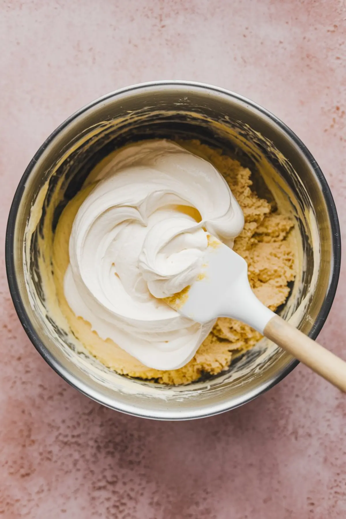 Partially mixed funfetti dip batter with whipped topping being folded into cake mix inside a stainless steel bowl with a white spatula.