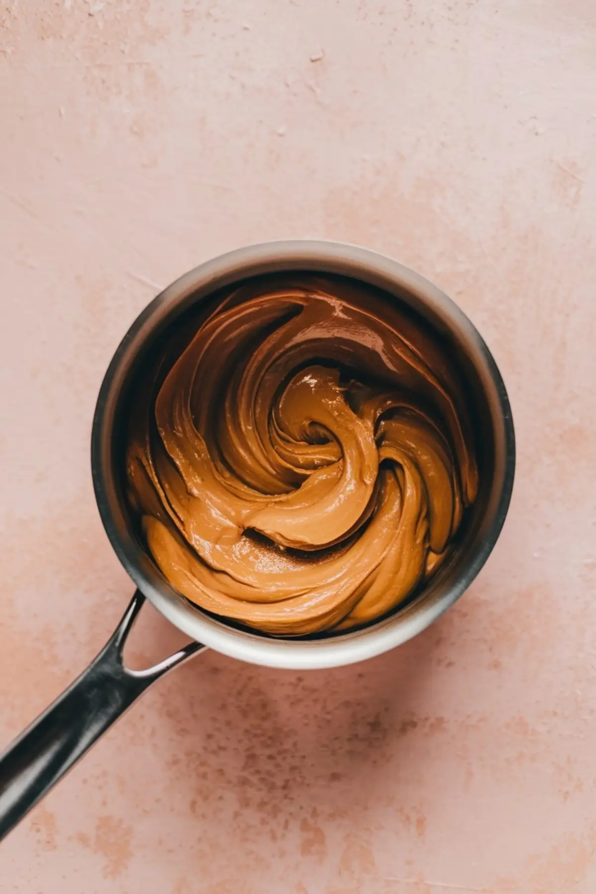 Top view of a saucepan filled with melted peanut butter chips swirled into a smooth, creamy consistency. The sauce forms the binding base for no-bake haystack clusters, contributing a rich and shiny finish.