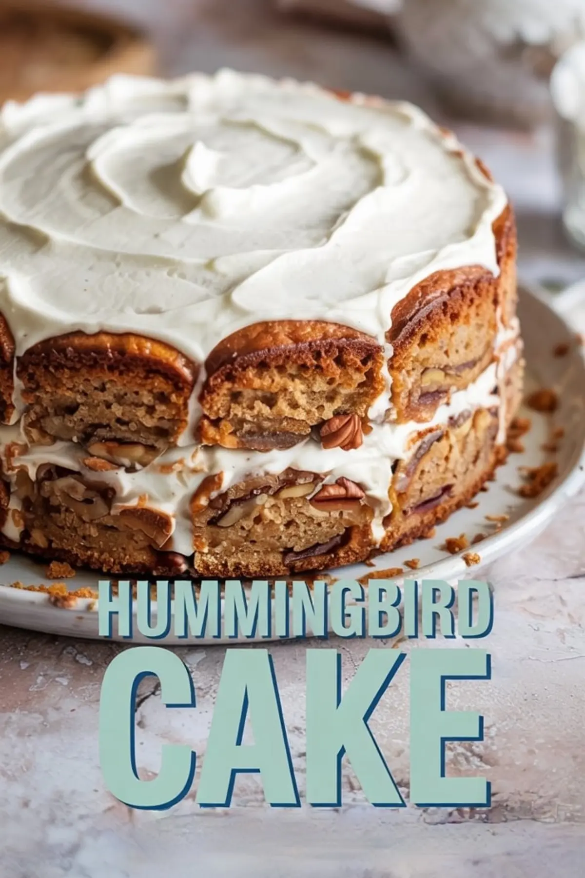 Frosted hummingbird cake decorated with cream cheese icing and toasted edges, displayed above a close-up slice showing layered banana-pineapple cake filled with pecans and fluffy cream cheese frosting.