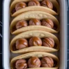 Tray of cookie tacos made with golden cookie shells, each filled with scoops of chocolate ice cream and topped with generous swirls of rich caramel sauce, arranged neatly on a dark marble background.