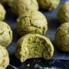Close-up of matcha no-bake balls with a cracked surface, featuring one bite-revealing soft green interior and bits of white chocolate.