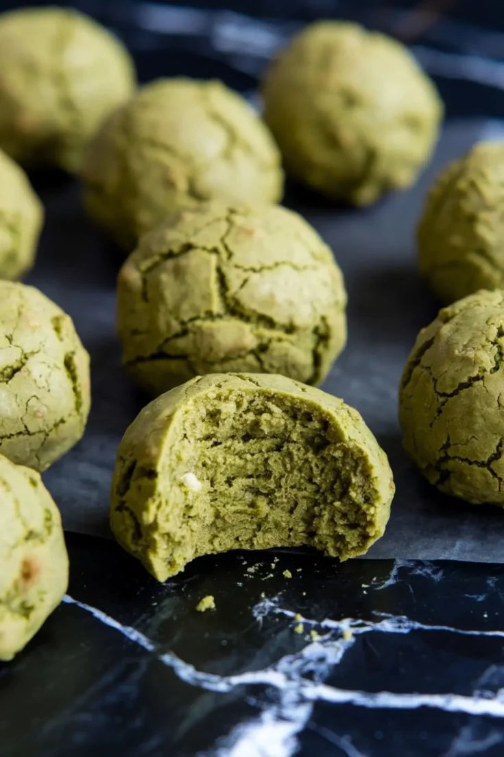 Close-up of matcha no-bake balls with a cracked surface, featuring one bite-revealing soft green interior and bits of white chocolate.