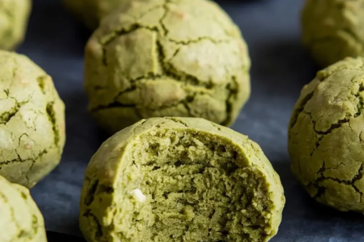 Close-up of matcha no-bake balls with a cracked surface, featuring one bite-revealing soft green interior and bits of white chocolate.