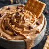 Creamy peanut butter cheesecake dip swirled in a ceramic bowl, topped with chocolate chips and crushed graham crackers, with graham crackers served on the side for dipping.