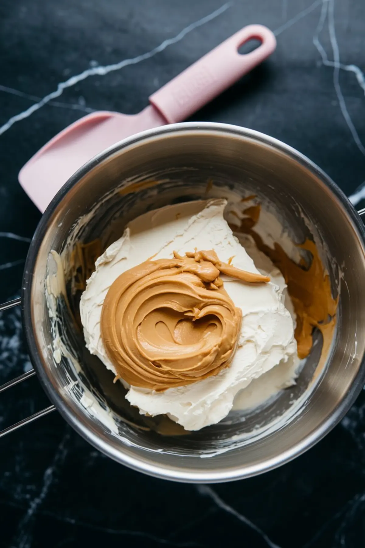 Stainless steel bowl holding softened cream cheese and creamy peanut butter, ready to be blended with a pink silicone spatula beside it.
