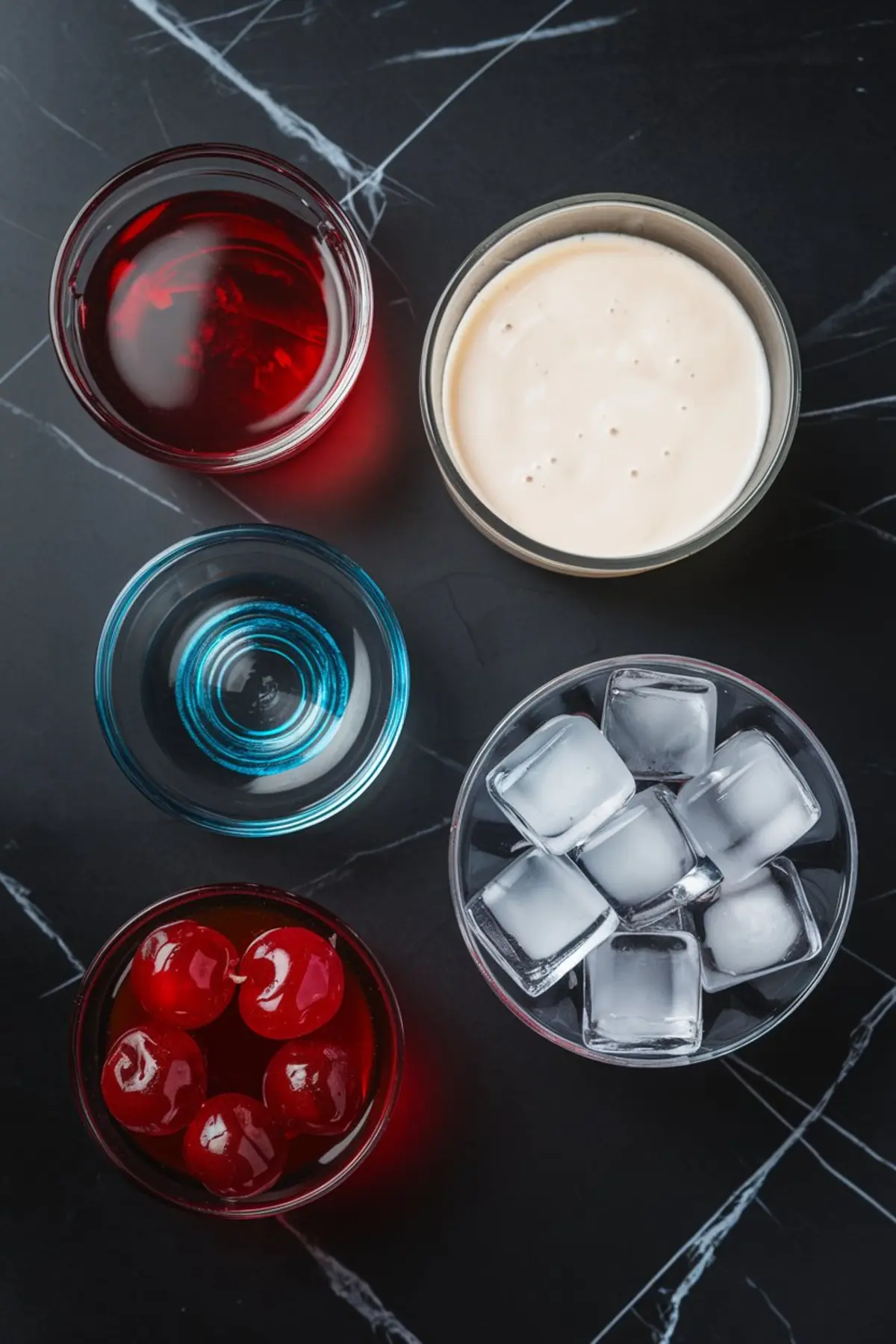 Flat lay of cocktail ingredients on a black marble background, including red grenadine, white cream liqueur, blue curaçao, maraschino cherries, ice cubes, and clear liquor, organized in small glass bowls.
