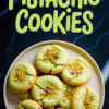 Overhead view of green pistachio cookies with cracked tops and chopped nuts, arranged on a white plate with bold text reading “Pistachio Cookies” on a dark marble surface.