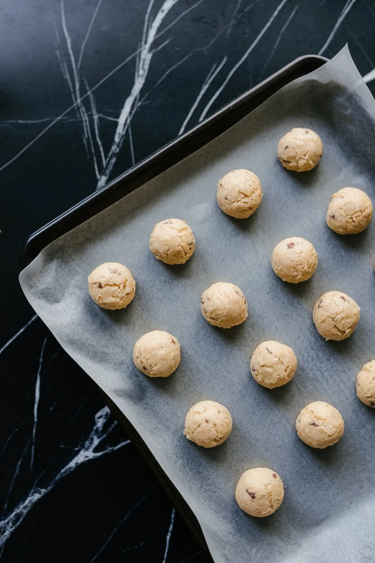 Unbaked cookie dough balls evenly spaced on a parchment-lined baking sheet, ready to go in the oven for cake mix cookies.